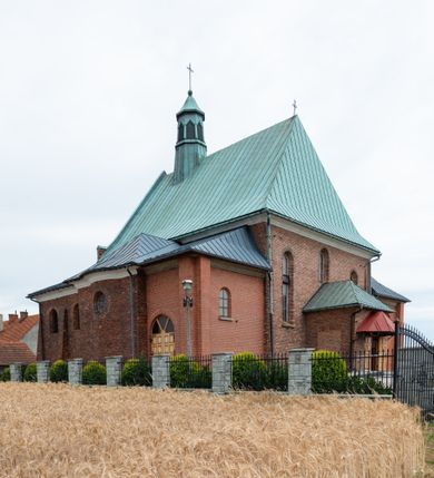 Zdjęcie nr 41: Kościół murowany z cegły na niskiej, kamiennej podmurówce, orientowany, jednonawowy ze zredukowanym transeptem oraz nieco niższym, zamkniętym półkoliście prezbiterium. Do północno-wschodniego narożnika nawy (przy prezbiterium) przylega założona na rzucie prostokąta, oszkarpowana zakrystia dostępna półkolistym portalem od strony północnej. Do południowo-wschodniego narożnika nawy dostawiona kaplica Matki Boskiej na rzucie prostokąta zamknięta od wschodu niewielką absydą. Ramiona transeptu zredukowane do roli prostokątnych kaplic. Do południowo-zachodniego i północno-zachodniego narożnika nawy dobudowane nowsze kruchty boczne założone na rzucie prostokąta dostępne portalami o półkolistym wykroju. Kruchta zachodnia na rzucie prostokąta dostępna nowym, prostokątnym wejściem. W ścianach północnej i południowej widoczne, zamurowane, starsze otwory wejściowe (od południa w miejsce portalu okrągłe okno). Dach nad nawą dwuspadowy z trzecią połacią zakrywającą ścianę szczytową; w części wschodniej wieloboczna wieżyczka na sygnaturkę z glorietą zwieńczoną krzyżem. Kruchty oraz kaplice boczne kryte dachami trójpołaciowymi, prezbiterium jednopołaciowym; nad zakrystią dach mansardowy z prostokątnym oknem w lukarnie. Pokrycia dachowe wykonane są z blachy (pierwotnie była to czerwona dachówka). W nawie i prezbiterium strop o konstrukcji żelbetowej wsparty na dziewięciu masywnych kolumnach ustawionych na wysokich cokołach; kaplice boczne sklepione krzyżowo, w zakrystii założony betonowy strop. Chór muzyczny murowany, wsparty na pierwszej od zachodu parze kolumn dźwigających strop. Fasada jednokondygnacyjna, trójosiowa z umieszczoną w osi centralnej prostopadłościenną kruchtą mieszczącą prostokątny otwór wejściowy (nowy). Okna w kształcie stojącego prostokąta o smukłych proporcjach, zamknięte półkoliście. Okno środkowe, umieszczone nieco wyżej, niższe od pozostałych. W ścianach zachodnich krucht bocznych po jednym niewielkim oknie o wykroju półkolistym. Trójkątna ściana szczytowa zasłonięta blaszanym dachem o przełamanej w dolnej części połaci, zwieńczona niewielkim, metalowym krzyżem. Elewacje boczne jednokondygnacyjne, o nieregularnym przebiegu osi. W elewacji południowej w pierwszej osi ceglany portal z nadświetlem o wykroju półkolistym, w drugiej okrągłe okno doświetlające kaplicę boczną, w kolejnych: półkolisty ceglany portal do zakrystii oraz okno o półkolistym wykroju z motywem biforium. W elewacji północnej w osi pierwszej i drugiej niewielkie półkoliście wykrojone okna, w osi trzeciej okrągłe okno doświetlające kaplicę, w osi czwartej natomiast ceglany portal  z nadświetlem o wykroju półkolistym. W prezbiterium cztery okna o wykroju półkolistym. W trzeciej osi, pomiędzy oknami, ujęta wielobocznymi filarami dźwigającymi, wydatny, profilowany gzyms tynkowana na biało nisza z figurą Matki Boskiej Fatimskiej umieszczonej pod baldachimem. Górną część murów nawy, prezbiterium, zakrystii, kaplic oraz obu krucht bocznych obiega profilowany gzyms okapowy. 