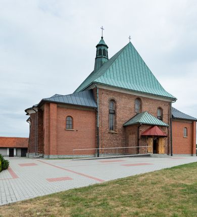 Zdjęcie nr 40: Kościół murowany z cegły na niskiej, kamiennej podmurówce, orientowany, jednonawowy ze zredukowanym transeptem oraz nieco niższym, zamkniętym półkoliście prezbiterium. Do północno-wschodniego narożnika nawy (przy prezbiterium) przylega założona na rzucie prostokąta, oszkarpowana zakrystia dostępna półkolistym portalem od strony północnej. Do południowo-wschodniego narożnika nawy dostawiona kaplica Matki Boskiej na rzucie prostokąta zamknięta od wschodu niewielką absydą. Ramiona transeptu zredukowane do roli prostokątnych kaplic. Do południowo-zachodniego i północno-zachodniego narożnika nawy dobudowane nowsze kruchty boczne założone na rzucie prostokąta dostępne portalami o półkolistym wykroju. Kruchta zachodnia na rzucie prostokąta dostępna nowym, prostokątnym wejściem. W ścianach północnej i południowej widoczne, zamurowane, starsze otwory wejściowe (od południa w miejsce portalu okrągłe okno). Dach nad nawą dwuspadowy z trzecią połacią zakrywającą ścianę szczytową; w części wschodniej wieloboczna wieżyczka na sygnaturkę z glorietą zwieńczoną krzyżem. Kruchty oraz kaplice boczne kryte dachami trójpołaciowymi, prezbiterium jednopołaciowym; nad zakrystią dach mansardowy z prostokątnym oknem w lukarnie. Pokrycia dachowe wykonane są z blachy (pierwotnie była to czerwona dachówka). W nawie i prezbiterium strop o konstrukcji żelbetowej wsparty na dziewięciu masywnych kolumnach ustawionych na wysokich cokołach; kaplice boczne sklepione krzyżowo, w zakrystii założony betonowy strop. Chór muzyczny murowany, wsparty na pierwszej od zachodu parze kolumn dźwigających strop. Fasada jednokondygnacyjna, trójosiowa z umieszczoną w osi centralnej prostopadłościenną kruchtą mieszczącą prostokątny otwór wejściowy (nowy). Okna w kształcie stojącego prostokąta o smukłych proporcjach, zamknięte półkoliście. Okno środkowe, umieszczone nieco wyżej, niższe od pozostałych. W ścianach zachodnich krucht bocznych po jednym niewielkim oknie o wykroju półkolistym. Trójkątna ściana szczytowa zasłonięta blaszanym dachem o przełamanej w dolnej części połaci, zwieńczona niewielkim, metalowym krzyżem. Elewacje boczne jednokondygnacyjne, o nieregularnym przebiegu osi. W elewacji południowej w pierwszej osi ceglany portal z nadświetlem o wykroju półkolistym, w drugiej okrągłe okno doświetlające kaplicę boczną, w kolejnych: półkolisty ceglany portal do zakrystii oraz okno o półkolistym wykroju z motywem biforium. W elewacji północnej w osi pierwszej i drugiej niewielkie półkoliście wykrojone okna, w osi trzeciej okrągłe okno doświetlające kaplicę, w osi czwartej natomiast ceglany portal  z nadświetlem o wykroju półkolistym. W prezbiterium cztery okna o wykroju półkolistym. W trzeciej osi, pomiędzy oknami, ujęta wielobocznymi filarami dźwigającymi, wydatny, profilowany gzyms tynkowana na biało nisza z figurą Matki Boskiej Fatimskiej umieszczonej pod baldachimem. Górną część murów nawy, prezbiterium, zakrystii, kaplic oraz obu krucht bocznych obiega profilowany gzyms okapowy. 
