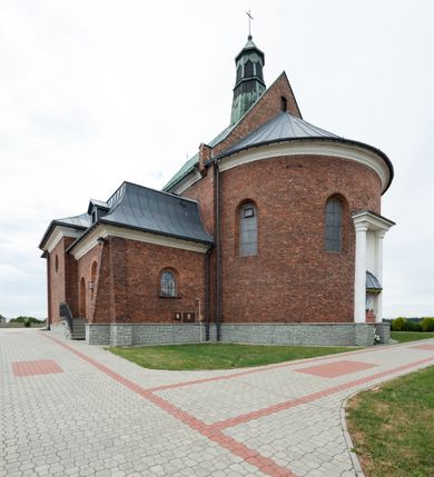 Zdjęcie nr 9: Kościół murowany z cegły na niskiej, kamiennej podmurówce, orientowany, jednonawowy ze zredukowanym transeptem oraz nieco niższym, zamkniętym półkoliście prezbiterium. Do północno-wschodniego narożnika nawy (przy prezbiterium) przylega założona na rzucie prostokąta, oszkarpowana zakrystia dostępna półkolistym portalem od strony północnej. Do południowo-wschodniego narożnika nawy dostawiona kaplica Matki Boskiej na rzucie prostokąta zamknięta od wschodu niewielką absydą. Ramiona transeptu zredukowane do roli prostokątnych kaplic. Do południowo-zachodniego i północno-zachodniego narożnika nawy dobudowane nowsze kruchty boczne założone na rzucie prostokąta dostępne portalami o półkolistym wykroju. Kruchta zachodnia na rzucie prostokąta dostępna nowym, prostokątnym wejściem. W ścianach północnej i południowej widoczne, zamurowane, starsze otwory wejściowe (od południa w miejsce portalu okrągłe okno). Dach nad nawą dwuspadowy z trzecią połacią zakrywającą ścianę szczytową; w części wschodniej wieloboczna wieżyczka na sygnaturkę z glorietą zwieńczoną krzyżem. Kruchty oraz kaplice boczne kryte dachami trójpołaciowymi, prezbiterium jednopołaciowym; nad zakrystią dach mansardowy z prostokątnym oknem w lukarnie. Pokrycia dachowe wykonane są z blachy (pierwotnie była to czerwona dachówka). W nawie i prezbiterium strop o konstrukcji żelbetowej wsparty na dziewięciu masywnych kolumnach ustawionych na wysokich cokołach; kaplice boczne sklepione krzyżowo, w zakrystii założony betonowy strop. Chór muzyczny murowany, wsparty na pierwszej od zachodu parze kolumn dźwigających strop. Fasada jednokondygnacyjna, trójosiowa z umieszczoną w osi centralnej prostopadłościenną kruchtą mieszczącą prostokątny otwór wejściowy (nowy). Okna w kształcie stojącego prostokąta o smukłych proporcjach, zamknięte półkoliście. Okno środkowe, umieszczone nieco wyżej, niższe od pozostałych. W ścianach zachodnich krucht bocznych po jednym niewielkim oknie o wykroju półkolistym. Trójkątna ściana szczytowa zasłonięta blaszanym dachem o przełamanej w dolnej części połaci, zwieńczona niewielkim, metalowym krzyżem. Elewacje boczne jednokondygnacyjne, o nieregularnym przebiegu osi. W elewacji południowej w pierwszej osi ceglany portal z nadświetlem o wykroju półkolistym, w drugiej okrągłe okno doświetlające kaplicę boczną, w kolejnych: półkolisty ceglany portal do zakrystii oraz okno o półkolistym wykroju z motywem biforium. W elewacji północnej w osi pierwszej i drugiej niewielkie półkoliście wykrojone okna, w osi trzeciej okrągłe okno doświetlające kaplicę, w osi czwartej natomiast ceglany portal  z nadświetlem o wykroju półkolistym. W prezbiterium cztery okna o wykroju półkolistym. W trzeciej osi, pomiędzy oknami, ujęta wielobocznymi filarami dźwigającymi, wydatny, profilowany gzyms tynkowana na biało nisza z figurą Matki Boskiej Fatimskiej umieszczonej pod baldachimem. Górną część murów nawy, prezbiterium, zakrystii, kaplic oraz obu krucht bocznych obiega profilowany gzyms okapowy. 