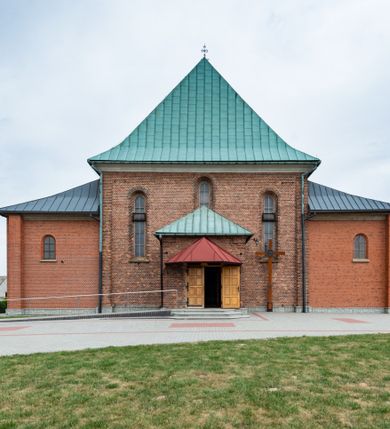 Zdjęcie nr 3: Kościół murowany z cegły na niskiej, kamiennej podmurówce, orientowany, jednonawowy ze zredukowanym transeptem oraz nieco niższym, zamkniętym półkoliście prezbiterium. Do północno-wschodniego narożnika nawy (przy prezbiterium) przylega założona na rzucie prostokąta, oszkarpowana zakrystia dostępna półkolistym portalem od strony północnej. Do południowo-wschodniego narożnika nawy dostawiona kaplica Matki Boskiej na rzucie prostokąta zamknięta od wschodu niewielką absydą. Ramiona transeptu zredukowane do roli prostokątnych kaplic. Do południowo-zachodniego i północno-zachodniego narożnika nawy dobudowane nowsze kruchty boczne założone na rzucie prostokąta dostępne portalami o półkolistym wykroju. Kruchta zachodnia na rzucie prostokąta dostępna nowym, prostokątnym wejściem. W ścianach północnej i południowej widoczne, zamurowane, starsze otwory wejściowe (od południa w miejsce portalu okrągłe okno). Dach nad nawą dwuspadowy z trzecią połacią zakrywającą ścianę szczytową; w części wschodniej wieloboczna wieżyczka na sygnaturkę z glorietą zwieńczoną krzyżem. Kruchty oraz kaplice boczne kryte dachami trójpołaciowymi, prezbiterium jednopołaciowym; nad zakrystią dach mansardowy z prostokątnym oknem w lukarnie. Pokrycia dachowe wykonane są z blachy (pierwotnie była to czerwona dachówka). W nawie i prezbiterium strop o konstrukcji żelbetowej wsparty na dziewięciu masywnych kolumnach ustawionych na wysokich cokołach; kaplice boczne sklepione krzyżowo, w zakrystii założony betonowy strop. Chór muzyczny murowany, wsparty na pierwszej od zachodu parze kolumn dźwigających strop. Fasada jednokondygnacyjna, trójosiowa z umieszczoną w osi centralnej prostopadłościenną kruchtą mieszczącą prostokątny otwór wejściowy (nowy). Okna w kształcie stojącego prostokąta o smukłych proporcjach, zamknięte półkoliście. Okno środkowe, umieszczone nieco wyżej, niższe od pozostałych. W ścianach zachodnich krucht bocznych po jednym niewielkim oknie o wykroju półkolistym. Trójkątna ściana szczytowa zasłonięta blaszanym dachem o przełamanej w dolnej części połaci, zwieńczona niewielkim, metalowym krzyżem. Elewacje boczne jednokondygnacyjne, o nieregularnym przebiegu osi. W elewacji południowej w pierwszej osi ceglany portal z nadświetlem o wykroju półkolistym, w drugiej okrągłe okno doświetlające kaplicę boczną, w kolejnych: półkolisty ceglany portal do zakrystii oraz okno o półkolistym wykroju z motywem biforium. W elewacji północnej w osi pierwszej i drugiej niewielkie półkoliście wykrojone okna, w osi trzeciej okrągłe okno doświetlające kaplicę, w osi czwartej natomiast ceglany portal  z nadświetlem o wykroju półkolistym. W prezbiterium cztery okna o wykroju półkolistym. W trzeciej osi, pomiędzy oknami, ujęta wielobocznymi filarami dźwigającymi, wydatny, profilowany gzyms tynkowana na biało nisza z figurą Matki Boskiej Fatimskiej umieszczonej pod baldachimem. Górną część murów nawy, prezbiterium, zakrystii, kaplic oraz obu krucht bocznych obiega profilowany gzyms okapowy. 