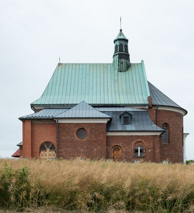 Zdjęcie nr 7: Kościół murowany z cegły na niskiej, kamiennej podmurówce, orientowany, jednonawowy ze zredukowanym transeptem oraz nieco niższym, zamkniętym półkoliście prezbiterium. Do północno-wschodniego narożnika nawy (przy prezbiterium) przylega założona na rzucie prostokąta, oszkarpowana zakrystia dostępna półkolistym portalem od strony północnej. Do południowo-wschodniego narożnika nawy dostawiona kaplica Matki Boskiej na rzucie prostokąta zamknięta od wschodu niewielką absydą. Ramiona transeptu zredukowane do roli prostokątnych kaplic. Do południowo-zachodniego i północno-zachodniego narożnika nawy dobudowane nowsze kruchty boczne założone na rzucie prostokąta dostępne portalami o półkolistym wykroju. Kruchta zachodnia na rzucie prostokąta dostępna nowym, prostokątnym wejściem. W ścianach północnej i południowej widoczne, zamurowane, starsze otwory wejściowe (od południa w miejsce portalu okrągłe okno). Dach nad nawą dwuspadowy z trzecią połacią zakrywającą ścianę szczytową; w części wschodniej wieloboczna wieżyczka na sygnaturkę z glorietą zwieńczoną krzyżem. Kruchty oraz kaplice boczne kryte dachami trójpołaciowymi, prezbiterium jednopołaciowym; nad zakrystią dach mansardowy z prostokątnym oknem w lukarnie. Pokrycia dachowe wykonane są z blachy (pierwotnie była to czerwona dachówka). W nawie i prezbiterium strop o konstrukcji żelbetowej wsparty na dziewięciu masywnych kolumnach ustawionych na wysokich cokołach; kaplice boczne sklepione krzyżowo, w zakrystii założony betonowy strop. Chór muzyczny murowany, wsparty na pierwszej od zachodu parze kolumn dźwigających strop. Fasada jednokondygnacyjna, trójosiowa z umieszczoną w osi centralnej prostopadłościenną kruchtą mieszczącą prostokątny otwór wejściowy (nowy). Okna w kształcie stojącego prostokąta o smukłych proporcjach, zamknięte półkoliście. Okno środkowe, umieszczone nieco wyżej, niższe od pozostałych. W ścianach zachodnich krucht bocznych po jednym niewielkim oknie o wykroju półkolistym. Trójkątna ściana szczytowa zasłonięta blaszanym dachem o przełamanej w dolnej części połaci, zwieńczona niewielkim, metalowym krzyżem. Elewacje boczne jednokondygnacyjne, o nieregularnym przebiegu osi. W elewacji południowej w pierwszej osi ceglany portal z nadświetlem o wykroju półkolistym, w drugiej okrągłe okno doświetlające kaplicę boczną, w kolejnych: półkolisty ceglany portal do zakrystii oraz okno o półkolistym wykroju z motywem biforium. W elewacji północnej w osi pierwszej i drugiej niewielkie półkoliście wykrojone okna, w osi trzeciej okrągłe okno doświetlające kaplicę, w osi czwartej natomiast ceglany portal  z nadświetlem o wykroju półkolistym. W prezbiterium cztery okna o wykroju półkolistym. W trzeciej osi, pomiędzy oknami, ujęta wielobocznymi filarami dźwigającymi, wydatny, profilowany gzyms tynkowana na biało nisza z figurą Matki Boskiej Fatimskiej umieszczonej pod baldachimem. Górną część murów nawy, prezbiterium, zakrystii, kaplic oraz obu krucht bocznych obiega profilowany gzyms okapowy. 