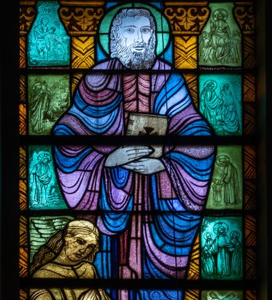 Zdjęcie nr 1: Witraż w kształcie stojącego prostokąta zamkniętego u góry łukiem półokrągłym. Kompozycja dwustrefowa. W dolnej części przedstawiony św. Mateusz ukazany frontalnie w ujęciu całopostaciowym. Święty wyobrażony jako dojrzały mężczyzna o dużych, ciemnych oczach i długim, prostym nosie. Włosy sięgające ramion i długa broda skręcone w spiralne loki. Postać ubrana w długą, czerwono-różową tunikę oraz płaszcz w odcieniach fioletu i błękitu, trzymająca w obu rękach zamkniętą księgę. Spod szat widoczne bose stopy. W dolnej części kompozycji widoczna klęcząca, długowłosa postać o dłoniach złożonych w geście modlitwy tj. anioł lub człowiek – symbol tego ewangelisty oraz banderola z napisem: „ŚW(IĘTY) MATEUSZ EWANGELISTA”. W tle widoczne wąskie romańskie kolumny o roślinnych kapitelach i trzonach dekorowanych geometryczną plecionką. W prześwitach pomiędzy kolumnami wkomponowano mniejsze sceny ukazujące wydarzenia związane z publiczną działalnością Chrystusa opisane przez św. Mateusza. W górnej części kompozycji w arkadzie ujętej dwiema zdwojonymi kolumienkami ukazany św. Szymon Apostoł trzymający w ręku narzędzie swojego męczeństwa – piłę. Święty ukazany frontalnie, w ujęciu całopostaciowym. Ubrany w beżową tunikę oraz jasnofioletowy płaszcz. Twarz owalna, włosy sięgające ramion, krótka broda. Arkada, w której umieszczono św. Szymona, ujęta jest dwoma mniejszymi arkadkami mieszczącymi motyw krzyża.