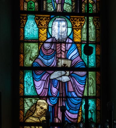 Zdjęcie nr 2: Witraż w kształcie stojącego prostokąta zamkniętego u góry łukiem półokrągłym. Kompozycja dwustrefowa. W dolnej części przedstawiony św. Mateusz ukazany frontalnie w ujęciu całopostaciowym. Święty wyobrażony jako dojrzały mężczyzna o dużych, ciemnych oczach i długim, prostym nosie. Włosy sięgające ramion i długa broda skręcone w spiralne loki. Postać ubrana w długą, czerwono-różową tunikę oraz płaszcz w odcieniach fioletu i błękitu, trzymająca w obu rękach zamkniętą księgę. Spod szat widoczne bose stopy. W dolnej części kompozycji widoczna klęcząca, długowłosa postać o dłoniach złożonych w geście modlitwy tj. anioł lub człowiek – symbol tego ewangelisty oraz banderola z napisem: „ŚW(IĘTY) MATEUSZ EWANGELISTA”. W tle widoczne wąskie romańskie kolumny o roślinnych kapitelach i trzonach dekorowanych geometryczną plecionką. W prześwitach pomiędzy kolumnami wkomponowano mniejsze sceny ukazujące wydarzenia związane z publiczną działalnością Chrystusa opisane przez św. Mateusza. W górnej części kompozycji w arkadzie ujętej dwiema zdwojonymi kolumienkami ukazany św. Szymon Apostoł trzymający w ręku narzędzie swojego męczeństwa – piłę. Święty ukazany frontalnie, w ujęciu całopostaciowym. Ubrany w beżową tunikę oraz jasnofioletowy płaszcz. Twarz owalna, włosy sięgające ramion, krótka broda. Arkada, w której umieszczono św. Szymona, ujęta jest dwoma mniejszymi arkadkami mieszczącymi motyw krzyża.