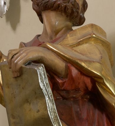 Zdjęcie nr 2: Święty został ukazany w całej postaci, z prawą nogą wspartą na pniu drzewa, w czerwonej sukni i złotym płaszczu okrywającym plecy i prawe biodro, z prawą ręką uniesioną, a lewą przytrzymującą księgę wspartą na biodrze. Głowa odchylona ku górze, z krótką brodą i krótkimi włosami, wydatnymi zakolami, z otwartymi oczami i ustami. 