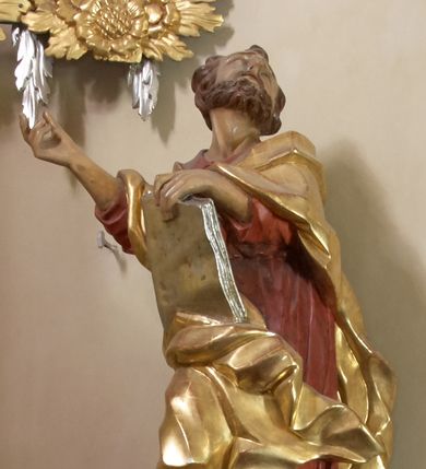 Zdjęcie nr 1: Święty został ukazany w całej postaci, z prawą nogą wspartą na pniu drzewa, w czerwonej sukni i złotym płaszczu okrywającym plecy i prawe biodro, z prawą ręką uniesioną, a lewą przytrzymującą księgę wspartą na biodrze. Głowa odchylona ku górze, z krótką brodą i krótkimi włosami, wydatnymi zakolami, z otwartymi oczami i ustami. 