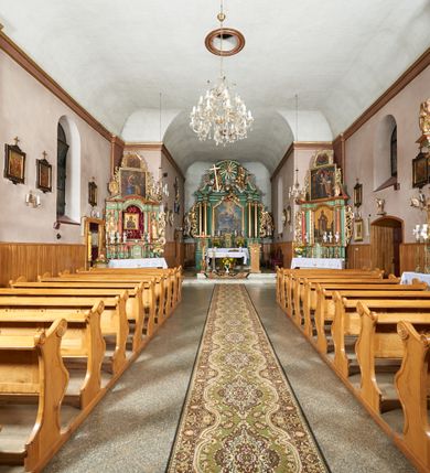 Zdjęcie nr 5: Kościół orientowany, murowany z kamienia i cegły, na planie prostokąta z szerszą nawą i węższym prezbiterium o zamknięciu wielobocznym, dobudowaną zakrystią, kruchtą od frontu i przedsionkiem od południa.  Od zachodu chór muzyczny z organami wsparty na dwóch kolumnach. Na ścianach iluzjonistyczne płyciny z fragmentami wici akantowej, glify we wnękach okiennych, na gzymsie ornament kostkowy, na stropie delikatna polichromia geometryczna z fragmentami wici akantowej. 
Nawa i prezbiterium przykryte stropem z głęboką fasetą imitującą sklepienie zwierciadlane, z oddzielającym je od partii ścian gzymsem. 
Otwory okienne w kształcie stojących prostokątów zakończonych półkoliście, różnej wielkości. Jedno okno w prezbiterium, po dwa z każdej strony nawy, dwa w kruchcie, dwa w fasadzie, a powyżej nich niewielki okulus. 
Główne wejście do kościoła od zachodu, przez kruchtę, kolejne od południa, przez przybudówkę, następne do zakrystii i do kotłowni.
Fasada została zakomponowana z dwóch części. Ściana kościoła jest zwieńczona trójkątnym szczytem ujętym niewysokimi murkami i zakończonym półokrągło, a przed jej lico wychodzi prostopadłościenna kruchta z małym, trójkątnym szczytem opracowanym podobnie jak szczyt fasady. 
Kościół ustawiony na cokole z kamienną okładziną. Elewacje zewnętrzne są gładkie, z podziałami lizenowo-ramowymi:  naroża podkreślone lizenami, kondygnacja oddzielona od partii dachu gzymsem podokapowym. 
Dachy dwuspadowe, kryte dachówką, na kalenicy nawy sześcioboczna wieżyczka na sygnaturkę z hełmem cebulastym krytym blachą. 