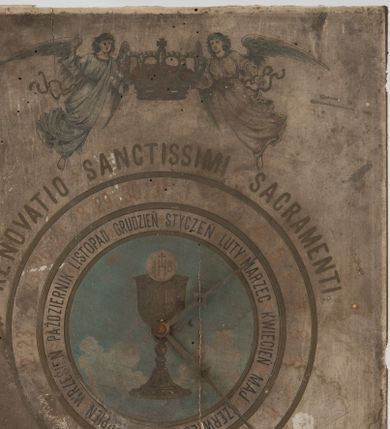 Zdjęcie nr 1: Zegar w kształcie stojącego prostokąta. W części centralnej okrągła tarcza, pośrodku kielich z hostią na tle błękitnego nieba, od którego odchodzą dwie fantazyjnie wycięte wskazówki. Wokół tarczy dwa okręgi, w pierwszym nazwy miesiąców, w drugim cyfry od 1 do 31. Powyżej napis „RENOVATIO * SANCTISSIMI * SACRAMENTI”, a nad nim dwa anioły podtrzymujące zamkniętą koronę. Anioły o owalnych twarzach, młodzieńczych rysach i średniej długości bujnych włosach. Ubrane w długie suknie z długimi rękawami, przewiązane w pasie wstążką. Rysunek oddany sumarycznie. W dolnej części kompozycji stylizowany, ornamentalny kartusz, w polu słaboczytelny napis i data „1906”. Poniżej sygnatury: „Nakładem K(azimierza) Zajączkowskiego w Krakowie.” oraz „Lit(itografia) A(?) S(D?)urczykiewicza w Krakowie.
