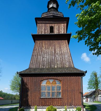 Zdjęcie nr 13: Kościół orientowany, drewniany, na podmurówce z kamienia łupanego, konstrukcji zrębowej, jednonawowy, szalowany, z wieżą konstrukcji słupowej usytuowaną od strony prezbiterium, z zakrystią w przyziemiu. Nawa prostokątna, szersza od prezbiterium, z kruchtami od zachodu, południa i północy. Prezbiterium zamknięte trójbocznie. Wieża od wschodu, na planie kwadratu, o konstrukcji ze słupów pochyłych, na zewnątrz trzy kondygnacje przedzielone obiegającymi daszkami. Dolna i górna izbica o ścianach pionowych, środkowa o ścianach pochyłych; wieża zwieńczona hełmem baniastym z latarnią. Kościół przykrywa dach siodłowy, na kruchtach trójspadowy, kryty cementówką. Pod wydatnymi okapami dachów biegnie gzyms o profilu ćwierćkoliście wklęsłym z wałkiem. Więźba dachowa nad prezbiterium jest krokwiowa, a nad nawą płatwiowa. Wewnątrz znajdują się stropy z fasetami, pod którymi umieszczony jest profilowany gzyms. Arkada tęczowa o łuku spłaszczonym. Chór muzyczny wsparty jest na dwóch filarach z wybrzuszoną balustradą. Wnętrze polichromowane, ściany w kruchtach oszalowane. Do kościoła prowadzą cztery wejścia: główne od zachodu, dwa boczne od południa i północy oraz przez zakrystię od wieży, od strony północno-zachodniej. W prezbiterium znajdują się dwa okna: po stronie południowej i północnej; a w nawie dwa po stronie południowej i północnej, natomiast w wieży cztery okna prostokątne, w latarni osiem okien zamkniętych dwoma nałęczami. Kościół otoczony jest murkiem ze stacjami drogi krzyżowej i dwiema bramkami z lat 1863 i 1864.
