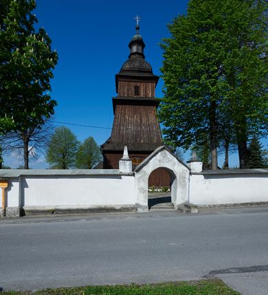 Zdjęcie nr 35: Kościół orientowany, drewniany, na podmurówce z kamienia łupanego, konstrukcji zrębowej, jednonawowy, szalowany, z wieżą konstrukcji słupowej usytuowaną od strony prezbiterium, z zakrystią w przyziemiu. Nawa prostokątna, szersza od prezbiterium, z kruchtami od zachodu, południa i północy. Prezbiterium zamknięte trójbocznie. Wieża od wschodu, na planie kwadratu, o konstrukcji ze słupów pochyłych, na zewnątrz trzy kondygnacje przedzielone obiegającymi daszkami. Dolna i górna izbica o ścianach pionowych, środkowa o ścianach pochyłych; wieża zwieńczona hełmem baniastym z latarnią. Kościół przykrywa dach siodłowy, na kruchtach trójspadowy, kryty cementówką. Pod wydatnymi okapami dachów biegnie gzyms o profilu ćwierćkoliście wklęsłym z wałkiem. Więźba dachowa nad prezbiterium jest krokwiowa, a nad nawą płatwiowa. Wewnątrz znajdują się stropy z fasetami, pod którymi umieszczony jest profilowany gzyms. Arkada tęczowa o łuku spłaszczonym. Chór muzyczny wsparty jest na dwóch filarach z wybrzuszoną balustradą. Wnętrze polichromowane, ściany w kruchtach oszalowane. Do kościoła prowadzą cztery wejścia: główne od zachodu, dwa boczne od południa i północy oraz przez zakrystię od wieży, od strony północno-zachodniej. W prezbiterium znajdują się dwa okna: po stronie południowej i północnej; a w nawie dwa po stronie południowej i północnej, natomiast w wieży cztery okna prostokątne, w latarni osiem okien zamkniętych dwoma nałęczami. Kościół otoczony jest murkiem ze stacjami drogi krzyżowej i dwiema bramkami z lat 1863 i 1864.