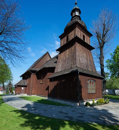 Zdjęcie nr 2: Kościół orientowany, drewniany, na podmurówce z kamienia łupanego, konstrukcji zrębowej, jednonawowy, szalowany, z wieżą konstrukcji słupowej usytuowaną od strony prezbiterium, z zakrystią w przyziemiu. Nawa prostokątna, szersza od prezbiterium, z kruchtami od zachodu, południa i północy. Prezbiterium zamknięte trójbocznie. Wieża od wschodu, na planie kwadratu, o konstrukcji ze słupów pochyłych, na zewnątrz trzy kondygnacje przedzielone obiegającymi daszkami. Dolna i górna izbica o ścianach pionowych, środkowa o ścianach pochyłych; wieża zwieńczona hełmem baniastym z latarnią. Kościół przykrywa dach siodłowy, na kruchtach trójspadowy, kryty cementówką. Pod wydatnymi okapami dachów biegnie gzyms o profilu ćwierćkoliście wklęsłym z wałkiem. Więźba dachowa nad prezbiterium jest krokwiowa, a nad nawą płatwiowa. Wewnątrz znajdują się stropy z fasetami, pod którymi umieszczony jest profilowany gzyms. Arkada tęczowa o łuku spłaszczonym. Chór muzyczny wsparty jest na dwóch filarach z wybrzuszoną balustradą. Wnętrze polichromowane, ściany w kruchtach oszalowane. Do kościoła prowadzą cztery wejścia: główne od zachodu, dwa boczne od południa i północy oraz przez zakrystię od wieży, od strony północno-zachodniej. W prezbiterium znajdują się dwa okna: po stronie południowej i północnej; a w nawie dwa po stronie południowej i północnej, natomiast w wieży cztery okna prostokątne, w latarni osiem okien zamkniętych dwoma nałęczami. Kościół otoczony jest murkiem ze stacjami drogi krzyżowej i dwiema bramkami z lat 1863 i 1864.