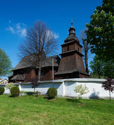 Zdjęcie nr 24: Kościół orientowany, drewniany, na podmurówce z kamienia łupanego, konstrukcji zrębowej, jednonawowy, szalowany, z wieżą konstrukcji słupowej usytuowaną od strony prezbiterium, z zakrystią w przyziemiu. Nawa prostokątna, szersza od prezbiterium, z kruchtami od zachodu, południa i północy. Prezbiterium zamknięte trójbocznie. Wieża od wschodu, na planie kwadratu, o konstrukcji ze słupów pochyłych, na zewnątrz trzy kondygnacje przedzielone obiegającymi daszkami. Dolna i górna izbica o ścianach pionowych, środkowa o ścianach pochyłych; wieża zwieńczona hełmem baniastym z latarnią. Kościół przykrywa dach siodłowy, na kruchtach trójspadowy, kryty cementówką. Pod wydatnymi okapami dachów biegnie gzyms o profilu ćwierćkoliście wklęsłym z wałkiem. Więźba dachowa nad prezbiterium jest krokwiowa, a nad nawą płatwiowa. Wewnątrz znajdują się stropy z fasetami, pod którymi umieszczony jest profilowany gzyms. Arkada tęczowa o łuku spłaszczonym. Chór muzyczny wsparty jest na dwóch filarach z wybrzuszoną balustradą. Wnętrze polichromowane, ściany w kruchtach oszalowane. Do kościoła prowadzą cztery wejścia: główne od zachodu, dwa boczne od południa i północy oraz przez zakrystię od wieży, od strony północno-zachodniej. W prezbiterium znajdują się dwa okna: po stronie południowej i północnej; a w nawie dwa po stronie południowej i północnej, natomiast w wieży cztery okna prostokątne, w latarni osiem okien zamkniętych dwoma nałęczami. Kościół otoczony jest murkiem ze stacjami drogi krzyżowej i dwiema bramkami z lat 1863 i 1864.