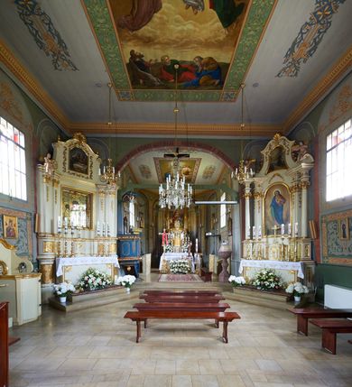 Zdjęcie nr 29: Kościół orientowany, drewniany, na podmurówce z kamienia łupanego, konstrukcji zrębowej, jednonawowy, szalowany, z wieżą konstrukcji słupowej usytuowaną od strony prezbiterium, z zakrystią w przyziemiu. Nawa prostokątna, szersza od prezbiterium, z kruchtami od zachodu, południa i północy. Prezbiterium zamknięte trójbocznie. Wieża od wschodu, na planie kwadratu, o konstrukcji ze słupów pochyłych, na zewnątrz trzy kondygnacje przedzielone obiegającymi daszkami. Dolna i górna izbica o ścianach pionowych, środkowa o ścianach pochyłych; wieża zwieńczona hełmem baniastym z latarnią. Kościół przykrywa dach siodłowy, na kruchtach trójspadowy, kryty cementówką. Pod wydatnymi okapami dachów biegnie gzyms o profilu ćwierćkoliście wklęsłym z wałkiem. Więźba dachowa nad prezbiterium jest krokwiowa, a nad nawą płatwiowa. Wewnątrz znajdują się stropy z fasetami, pod którymi umieszczony jest profilowany gzyms. Arkada tęczowa o łuku spłaszczonym. Chór muzyczny wsparty jest na dwóch filarach z wybrzuszoną balustradą. Wnętrze polichromowane, ściany w kruchtach oszalowane. Do kościoła prowadzą cztery wejścia: główne od zachodu, dwa boczne od południa i północy oraz przez zakrystię od wieży, od strony północno-zachodniej. W prezbiterium znajdują się dwa okna: po stronie południowej i północnej; a w nawie dwa po stronie południowej i północnej, natomiast w wieży cztery okna prostokątne, w latarni osiem okien zamkniętych dwoma nałęczami. Kościół otoczony jest murkiem ze stacjami drogi krzyżowej i dwiema bramkami z lat 1863 i 1864.