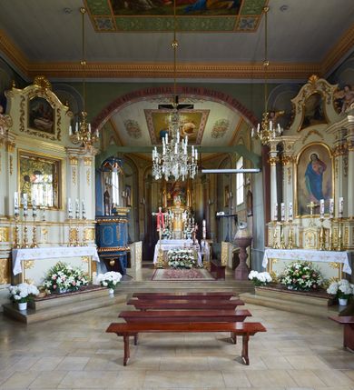 Zdjęcie nr 28: Kościół orientowany, drewniany, na podmurówce z kamienia łupanego, konstrukcji zrębowej, jednonawowy, szalowany, z wieżą konstrukcji słupowej usytuowaną od strony prezbiterium, z zakrystią w przyziemiu. Nawa prostokątna, szersza od prezbiterium, z kruchtami od zachodu, południa i północy. Prezbiterium zamknięte trójbocznie. Wieża od wschodu, na planie kwadratu, o konstrukcji ze słupów pochyłych, na zewnątrz trzy kondygnacje przedzielone obiegającymi daszkami. Dolna i górna izbica o ścianach pionowych, środkowa o ścianach pochyłych; wieża zwieńczona hełmem baniastym z latarnią. Kościół przykrywa dach siodłowy, na kruchtach trójspadowy, kryty cementówką. Pod wydatnymi okapami dachów biegnie gzyms o profilu ćwierćkoliście wklęsłym z wałkiem. Więźba dachowa nad prezbiterium jest krokwiowa, a nad nawą płatwiowa. Wewnątrz znajdują się stropy z fasetami, pod którymi umieszczony jest profilowany gzyms. Arkada tęczowa o łuku spłaszczonym. Chór muzyczny wsparty jest na dwóch filarach z wybrzuszoną balustradą. Wnętrze polichromowane, ściany w kruchtach oszalowane. Do kościoła prowadzą cztery wejścia: główne od zachodu, dwa boczne od południa i północy oraz przez zakrystię od wieży, od strony północno-zachodniej. W prezbiterium znajdują się dwa okna: po stronie południowej i północnej; a w nawie dwa po stronie południowej i północnej, natomiast w wieży cztery okna prostokątne, w latarni osiem okien zamkniętych dwoma nałęczami. Kościół otoczony jest murkiem ze stacjami drogi krzyżowej i dwiema bramkami z lat 1863 i 1864.