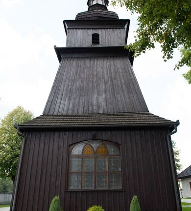 Zdjęcie nr 38: Kościół orientowany, drewniany, na podmurówce z kamienia łupanego, konstrukcji zrębowej, jednonawowy, szalowany, z wieżą konstrukcji słupowej usytuowaną od strony prezbiterium, z zakrystią w przyziemiu. Nawa prostokątna, szersza od prezbiterium, z kruchtami od zachodu, południa i północy. Prezbiterium zamknięte trójbocznie. Wieża od wschodu, na planie kwadratu, o konstrukcji ze słupów pochyłych, na zewnątrz trzy kondygnacje przedzielone obiegającymi daszkami. Dolna i górna izbica o ścianach pionowych, środkowa o ścianach pochyłych; wieża zwieńczona hełmem baniastym z latarnią. Kościół przykrywa dach siodłowy, na kruchtach trójspadowy, kryty cementówką. Pod wydatnymi okapami dachów biegnie gzyms o profilu ćwierćkoliście wklęsłym z wałkiem. Więźba dachowa nad prezbiterium jest krokwiowa, a nad nawą płatwiowa. Wewnątrz znajdują się stropy z fasetami, pod którymi umieszczony jest profilowany gzyms. Arkada tęczowa o łuku spłaszczonym. Chór muzyczny wsparty jest na dwóch filarach z wybrzuszoną balustradą. Wnętrze polichromowane, ściany w kruchtach oszalowane. Do kościoła prowadzą cztery wejścia: główne od zachodu, dwa boczne od południa i północy oraz przez zakrystię od wieży, od strony północno-zachodniej. W prezbiterium znajdują się dwa okna: po stronie południowej i północnej; a w nawie dwa po stronie południowej i północnej, natomiast w wieży cztery okna prostokątne, w latarni osiem okien zamkniętych dwoma nałęczami. Kościół otoczony jest murkiem ze stacjami drogi krzyżowej i dwiema bramkami z lat 1863 i 1864.