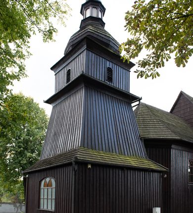 Zdjęcie nr 36: Kościół orientowany, drewniany, na podmurówce z kamienia łupanego, konstrukcji zrębowej, jednonawowy, szalowany, z wieżą konstrukcji słupowej usytuowaną od strony prezbiterium, z zakrystią w przyziemiu. Nawa prostokątna, szersza od prezbiterium, z kruchtami od zachodu, południa i północy. Prezbiterium zamknięte trójbocznie. Wieża od wschodu, na planie kwadratu, o konstrukcji ze słupów pochyłych, na zewnątrz trzy kondygnacje przedzielone obiegającymi daszkami. Dolna i górna izbica o ścianach pionowych, środkowa o ścianach pochyłych; wieża zwieńczona hełmem baniastym z latarnią. Kościół przykrywa dach siodłowy, na kruchtach trójspadowy, kryty cementówką. Pod wydatnymi okapami dachów biegnie gzyms o profilu ćwierćkoliście wklęsłym z wałkiem. Więźba dachowa nad prezbiterium jest krokwiowa, a nad nawą płatwiowa. Wewnątrz znajdują się stropy z fasetami, pod którymi umieszczony jest profilowany gzyms. Arkada tęczowa o łuku spłaszczonym. Chór muzyczny wsparty jest na dwóch filarach z wybrzuszoną balustradą. Wnętrze polichromowane, ściany w kruchtach oszalowane. Do kościoła prowadzą cztery wejścia: główne od zachodu, dwa boczne od południa i północy oraz przez zakrystię od wieży, od strony północno-zachodniej. W prezbiterium znajdują się dwa okna: po stronie południowej i północnej; a w nawie dwa po stronie południowej i północnej, natomiast w wieży cztery okna prostokątne, w latarni osiem okien zamkniętych dwoma nałęczami. Kościół otoczony jest murkiem ze stacjami drogi krzyżowej i dwiema bramkami z lat 1863 i 1864.