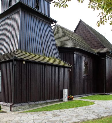 Zdjęcie nr 37: Kościół orientowany, drewniany, na podmurówce z kamienia łupanego, konstrukcji zrębowej, jednonawowy, szalowany, z wieżą konstrukcji słupowej usytuowaną od strony prezbiterium, z zakrystią w przyziemiu. Nawa prostokątna, szersza od prezbiterium, z kruchtami od zachodu, południa i północy. Prezbiterium zamknięte trójbocznie. Wieża od wschodu, na planie kwadratu, o konstrukcji ze słupów pochyłych, na zewnątrz trzy kondygnacje przedzielone obiegającymi daszkami. Dolna i górna izbica o ścianach pionowych, środkowa o ścianach pochyłych; wieża zwieńczona hełmem baniastym z latarnią. Kościół przykrywa dach siodłowy, na kruchtach trójspadowy, kryty cementówką. Pod wydatnymi okapami dachów biegnie gzyms o profilu ćwierćkoliście wklęsłym z wałkiem. Więźba dachowa nad prezbiterium jest krokwiowa, a nad nawą płatwiowa. Wewnątrz znajdują się stropy z fasetami, pod którymi umieszczony jest profilowany gzyms. Arkada tęczowa o łuku spłaszczonym. Chór muzyczny wsparty jest na dwóch filarach z wybrzuszoną balustradą. Wnętrze polichromowane, ściany w kruchtach oszalowane. Do kościoła prowadzą cztery wejścia: główne od zachodu, dwa boczne od południa i północy oraz przez zakrystię od wieży, od strony północno-zachodniej. W prezbiterium znajdują się dwa okna: po stronie południowej i północnej; a w nawie dwa po stronie południowej i północnej, natomiast w wieży cztery okna prostokątne, w latarni osiem okien zamkniętych dwoma nałęczami. Kościół otoczony jest murkiem ze stacjami drogi krzyżowej i dwiema bramkami z lat 1863 i 1864.