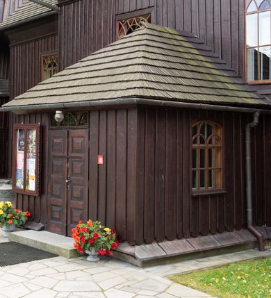 Zdjęcie nr 6: Kościół orientowany, drewniany, na podmurówce z kamienia łupanego, konstrukcji zrębowej, jednonawowy, szalowany, z wieżą konstrukcji słupowej usytuowaną od strony prezbiterium, z zakrystią w przyziemiu. Nawa prostokątna, szersza od prezbiterium, z kruchtami od zachodu, południa i północy. Prezbiterium zamknięte trójbocznie. Wieża od wschodu, na planie kwadratu, o konstrukcji ze słupów pochyłych, na zewnątrz trzy kondygnacje przedzielone obiegającymi daszkami. Dolna i górna izbica o ścianach pionowych, środkowa o ścianach pochyłych; wieża zwieńczona hełmem baniastym z latarnią. Kościół przykrywa dach siodłowy, na kruchtach trójspadowy, kryty cementówką. Pod wydatnymi okapami dachów biegnie gzyms o profilu ćwierćkoliście wklęsłym z wałkiem. Więźba dachowa nad prezbiterium jest krokwiowa, a nad nawą płatwiowa. Wewnątrz znajdują się stropy z fasetami, pod którymi umieszczony jest profilowany gzyms. Arkada tęczowa o łuku spłaszczonym. Chór muzyczny wsparty jest na dwóch filarach z wybrzuszoną balustradą. Wnętrze polichromowane, ściany w kruchtach oszalowane. Do kościoła prowadzą cztery wejścia: główne od zachodu, dwa boczne od południa i północy oraz przez zakrystię od wieży, od strony północno-zachodniej. W prezbiterium znajdują się dwa okna: po stronie południowej i północnej; a w nawie dwa po stronie południowej i północnej, natomiast w wieży cztery okna prostokątne, w latarni osiem okien zamkniętych dwoma nałęczami. Kościół otoczony jest murkiem ze stacjami drogi krzyżowej i dwiema bramkami z lat 1863 i 1864.