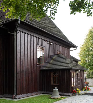 Zdjęcie nr 5: Kościół orientowany, drewniany, na podmurówce z kamienia łupanego, konstrukcji zrębowej, jednonawowy, szalowany, z wieżą konstrukcji słupowej usytuowaną od strony prezbiterium, z zakrystią w przyziemiu. Nawa prostokątna, szersza od prezbiterium, z kruchtami od zachodu, południa i północy. Prezbiterium zamknięte trójbocznie. Wieża od wschodu, na planie kwadratu, o konstrukcji ze słupów pochyłych, na zewnątrz trzy kondygnacje przedzielone obiegającymi daszkami. Dolna i górna izbica o ścianach pionowych, środkowa o ścianach pochyłych; wieża zwieńczona hełmem baniastym z latarnią. Kościół przykrywa dach siodłowy, na kruchtach trójspadowy, kryty cementówką. Pod wydatnymi okapami dachów biegnie gzyms o profilu ćwierćkoliście wklęsłym z wałkiem. Więźba dachowa nad prezbiterium jest krokwiowa, a nad nawą płatwiowa. Wewnątrz znajdują się stropy z fasetami, pod którymi umieszczony jest profilowany gzyms. Arkada tęczowa o łuku spłaszczonym. Chór muzyczny wsparty jest na dwóch filarach z wybrzuszoną balustradą. Wnętrze polichromowane, ściany w kruchtach oszalowane. Do kościoła prowadzą cztery wejścia: główne od zachodu, dwa boczne od południa i północy oraz przez zakrystię od wieży, od strony północno-zachodniej. W prezbiterium znajdują się dwa okna: po stronie południowej i północnej; a w nawie dwa po stronie południowej i północnej, natomiast w wieży cztery okna prostokątne, w latarni osiem okien zamkniętych dwoma nałęczami. Kościół otoczony jest murkiem ze stacjami drogi krzyżowej i dwiema bramkami z lat 1863 i 1864.