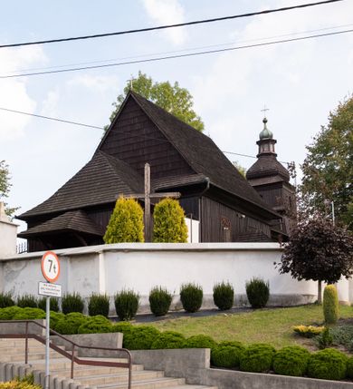 Zdjęcie nr 17: Kościół orientowany, drewniany, na podmurówce z kamienia łupanego, konstrukcji zrębowej, jednonawowy, szalowany, z wieżą konstrukcji słupowej usytuowaną od strony prezbiterium, z zakrystią w przyziemiu. Nawa prostokątna, szersza od prezbiterium, z kruchtami od zachodu, południa i północy. Prezbiterium zamknięte trójbocznie. Wieża od wschodu, na planie kwadratu, o konstrukcji ze słupów pochyłych, na zewnątrz trzy kondygnacje przedzielone obiegającymi daszkami. Dolna i górna izbica o ścianach pionowych, środkowa o ścianach pochyłych; wieża zwieńczona hełmem baniastym z latarnią. Kościół przykrywa dach siodłowy, na kruchtach trójspadowy, kryty cementówką. Pod wydatnymi okapami dachów biegnie gzyms o profilu ćwierćkoliście wklęsłym z wałkiem. Więźba dachowa nad prezbiterium jest krokwiowa, a nad nawą płatwiowa. Wewnątrz znajdują się stropy z fasetami, pod którymi umieszczony jest profilowany gzyms. Arkada tęczowa o łuku spłaszczonym. Chór muzyczny wsparty jest na dwóch filarach z wybrzuszoną balustradą. Wnętrze polichromowane, ściany w kruchtach oszalowane. Do kościoła prowadzą cztery wejścia: główne od zachodu, dwa boczne od południa i północy oraz przez zakrystię od wieży, od strony północno-zachodniej. W prezbiterium znajdują się dwa okna: po stronie południowej i północnej; a w nawie dwa po stronie południowej i północnej, natomiast w wieży cztery okna prostokątne, w latarni osiem okien zamkniętych dwoma nałęczami. Kościół otoczony jest murkiem ze stacjami drogi krzyżowej i dwiema bramkami z lat 1863 i 1864.