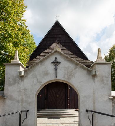 Zdjęcie nr 18: Kościół orientowany, drewniany, na podmurówce z kamienia łupanego, konstrukcji zrębowej, jednonawowy, szalowany, z wieżą konstrukcji słupowej usytuowaną od strony prezbiterium, z zakrystią w przyziemiu. Nawa prostokątna, szersza od prezbiterium, z kruchtami od zachodu, południa i północy. Prezbiterium zamknięte trójbocznie. Wieża od wschodu, na planie kwadratu, o konstrukcji ze słupów pochyłych, na zewnątrz trzy kondygnacje przedzielone obiegającymi daszkami. Dolna i górna izbica o ścianach pionowych, środkowa o ścianach pochyłych; wieża zwieńczona hełmem baniastym z latarnią. Kościół przykrywa dach siodłowy, na kruchtach trójspadowy, kryty cementówką. Pod wydatnymi okapami dachów biegnie gzyms o profilu ćwierćkoliście wklęsłym z wałkiem. Więźba dachowa nad prezbiterium jest krokwiowa, a nad nawą płatwiowa. Wewnątrz znajdują się stropy z fasetami, pod którymi umieszczony jest profilowany gzyms. Arkada tęczowa o łuku spłaszczonym. Chór muzyczny wsparty jest na dwóch filarach z wybrzuszoną balustradą. Wnętrze polichromowane, ściany w kruchtach oszalowane. Do kościoła prowadzą cztery wejścia: główne od zachodu, dwa boczne od południa i północy oraz przez zakrystię od wieży, od strony północno-zachodniej. W prezbiterium znajdują się dwa okna: po stronie południowej i północnej; a w nawie dwa po stronie południowej i północnej, natomiast w wieży cztery okna prostokątne, w latarni osiem okien zamkniętych dwoma nałęczami. Kościół otoczony jest murkiem ze stacjami drogi krzyżowej i dwiema bramkami z lat 1863 i 1864.