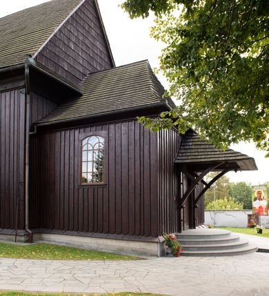 Zdjęcie nr 11: Kościół orientowany, drewniany, na podmurówce z kamienia łupanego, konstrukcji zrębowej, jednonawowy, szalowany, z wieżą konstrukcji słupowej usytuowaną od strony prezbiterium, z zakrystią w przyziemiu. Nawa prostokątna, szersza od prezbiterium, z kruchtami od zachodu, południa i północy. Prezbiterium zamknięte trójbocznie. Wieża od wschodu, na planie kwadratu, o konstrukcji ze słupów pochyłych, na zewnątrz trzy kondygnacje przedzielone obiegającymi daszkami. Dolna i górna izbica o ścianach pionowych, środkowa o ścianach pochyłych; wieża zwieńczona hełmem baniastym z latarnią. Kościół przykrywa dach siodłowy, na kruchtach trójspadowy, kryty cementówką. Pod wydatnymi okapami dachów biegnie gzyms o profilu ćwierćkoliście wklęsłym z wałkiem. Więźba dachowa nad prezbiterium jest krokwiowa, a nad nawą płatwiowa. Wewnątrz znajdują się stropy z fasetami, pod którymi umieszczony jest profilowany gzyms. Arkada tęczowa o łuku spłaszczonym. Chór muzyczny wsparty jest na dwóch filarach z wybrzuszoną balustradą. Wnętrze polichromowane, ściany w kruchtach oszalowane. Do kościoła prowadzą cztery wejścia: główne od zachodu, dwa boczne od południa i północy oraz przez zakrystię od wieży, od strony północno-zachodniej. W prezbiterium znajdują się dwa okna: po stronie południowej i północnej; a w nawie dwa po stronie południowej i północnej, natomiast w wieży cztery okna prostokątne, w latarni osiem okien zamkniętych dwoma nałęczami. Kościół otoczony jest murkiem ze stacjami drogi krzyżowej i dwiema bramkami z lat 1863 i 1864.