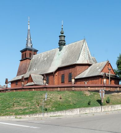 Zdjęcie nr 3: Kościół Przemienienia Pańskiego w Radoczy usytuowany jest w centrum wsi na zachód od głównej drogi prowadzącej z Wadowic do Zatora. Teren przykościelny jest usytuowany na niewielkim wzniesieniu, otoczony drewnianym płotem. Główne wejście na plac przykościelny prowadzi przez bramę od strony zachodniej.

Kościół jest orientowany, drewniany o konstrukcji zrębowej z wieżą na słup, jednonawowy z krótszym prezbiterium zamkniętym trójbocznie. Przy prezbiterium od wschodu nowsza zakrystia murowana, od północy kaplica i składzik, przy nawie od południa kruchta. Wnętrze nakryte pułapem, w nawie z zaskrzynieniami. Ściana arkady tęczowej o wykroju prostokątnym ze ściętymi narożami. Do kościoła prowadzi główne wejście w wieży od strony północnej. Wnętrze świątyni oświetlają prostokątne okna od strony południowej. Dach o jednej kalenicy, kryty blachą, na środku drewniana sygnaturka, nakryta kopułką z latarnią.  Od zachodu wieża w dolnej kondygnacji na planie prostokąta, ujęta po bokach daszkami; druga kondygnacja o ścianach pochyłych, pokryta gontem; trzecia kondygnacja prześwietlona prostokątnymi otworami okiennymi; wieża zakończona iglicą. Ściany na zewnątrz pokryte szalunkiem pionowym.
