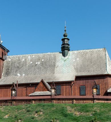 Zdjęcie nr 4: Kościół Przemienienia Pańskiego w Radoczy usytuowany jest w centrum wsi na zachód od głównej drogi prowadzącej z Wadowic do Zatora. Teren przykościelny jest usytuowany na niewielkim wzniesieniu, otoczony drewnianym płotem. Główne wejście na plac przykościelny prowadzi przez bramę od strony zachodniej.

Kościół jest orientowany, drewniany o konstrukcji zrębowej z wieżą na słup, jednonawowy z krótszym prezbiterium zamkniętym trójbocznie. Przy prezbiterium od wschodu nowsza zakrystia murowana, od północy kaplica i składzik, przy nawie od południa kruchta. Wnętrze nakryte pułapem, w nawie z zaskrzynieniami. Ściana arkady tęczowej o wykroju prostokątnym ze ściętymi narożami. Do kościoła prowadzi główne wejście w wieży od strony północnej. Wnętrze świątyni oświetlają prostokątne okna od strony południowej. Dach o jednej kalenicy, kryty blachą, na środku drewniana sygnaturka, nakryta kopułką z latarnią.  Od zachodu wieża w dolnej kondygnacji na planie prostokąta, ujęta po bokach daszkami; druga kondygnacja o ścianach pochyłych, pokryta gontem; trzecia kondygnacja prześwietlona prostokątnymi otworami okiennymi; wieża zakończona iglicą. Ściany na zewnątrz pokryte szalunkiem pionowym.
