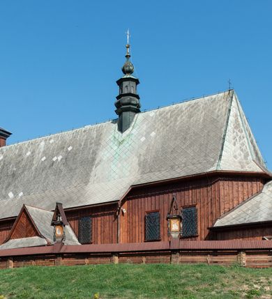 Zdjęcie nr 5: Kościół Przemienienia Pańskiego w Radoczy usytuowany jest w centrum wsi na zachód od głównej drogi prowadzącej z Wadowic do Zatora. Teren przykościelny jest usytuowany na niewielkim wzniesieniu, otoczony drewnianym płotem. Główne wejście na plac przykościelny prowadzi przez bramę od strony zachodniej.

Kościół jest orientowany, drewniany o konstrukcji zrębowej z wieżą na słup, jednonawowy z krótszym prezbiterium zamkniętym trójbocznie. Przy prezbiterium od wschodu nowsza zakrystia murowana, od północy kaplica i składzik, przy nawie od południa kruchta. Wnętrze nakryte pułapem, w nawie z zaskrzynieniami. Ściana arkady tęczowej o wykroju prostokątnym ze ściętymi narożami. Do kościoła prowadzi główne wejście w wieży od strony północnej. Wnętrze świątyni oświetlają prostokątne okna od strony południowej. Dach o jednej kalenicy, kryty blachą, na środku drewniana sygnaturka, nakryta kopułką z latarnią.  Od zachodu wieża w dolnej kondygnacji na planie prostokąta, ujęta po bokach daszkami; druga kondygnacja o ścianach pochyłych, pokryta gontem; trzecia kondygnacja prześwietlona prostokątnymi otworami okiennymi; wieża zakończona iglicą. Ściany na zewnątrz pokryte szalunkiem pionowym.
