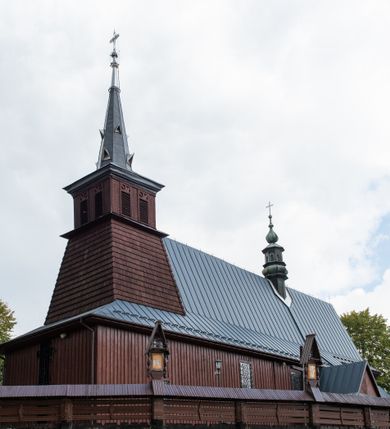 Zdjęcie nr 12: Kościół Przemienienia Pańskiego w Radoczy usytuowany jest w centrum wsi na zachód od głównej drogi prowadzącej z Wadowic do Zatora. Teren przykościelny jest usytuowany na niewielkim wzniesieniu, otoczony drewnianym płotem. Główne wejście na plac przykościelny prowadzi przez bramę od strony zachodniej.

Kościół jest orientowany, drewniany o konstrukcji zrębowej z wieżą na słup, jednonawowy z krótszym prezbiterium zamkniętym trójbocznie. Przy prezbiterium od wschodu nowsza zakrystia murowana, od północy kaplica i składzik, przy nawie od południa kruchta. Wnętrze nakryte pułapem, w nawie z zaskrzynieniami. Ściana arkady tęczowej o wykroju prostokątnym ze ściętymi narożami. Do kościoła prowadzi główne wejście w wieży od strony północnej. Wnętrze świątyni oświetlają prostokątne okna od strony południowej. Dach o jednej kalenicy, kryty blachą, na środku drewniana sygnaturka, nakryta kopułką z latarnią.  Od zachodu wieża w dolnej kondygnacji na planie prostokąta, ujęta po bokach daszkami; druga kondygnacja o ścianach pochyłych, pokryta gontem; trzecia kondygnacja prześwietlona prostokątnymi otworami okiennymi; wieża zakończona iglicą. Ściany na zewnątrz pokryte szalunkiem pionowym.
