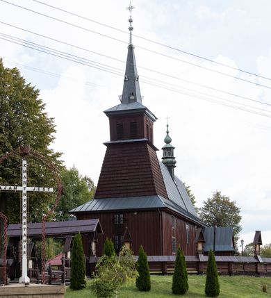 Zdjęcie nr 11: Kościół Przemienienia Pańskiego w Radoczy usytuowany jest w centrum wsi na zachód od głównej drogi prowadzącej z Wadowic do Zatora. Teren przykościelny jest usytuowany na niewielkim wzniesieniu, otoczony drewnianym płotem. Główne wejście na plac przykościelny prowadzi przez bramę od strony zachodniej.

Kościół jest orientowany, drewniany o konstrukcji zrębowej z wieżą na słup, jednonawowy z krótszym prezbiterium zamkniętym trójbocznie. Przy prezbiterium od wschodu nowsza zakrystia murowana, od północy kaplica i składzik, przy nawie od południa kruchta. Wnętrze nakryte pułapem, w nawie z zaskrzynieniami. Ściana arkady tęczowej o wykroju prostokątnym ze ściętymi narożami. Do kościoła prowadzi główne wejście w wieży od strony północnej. Wnętrze świątyni oświetlają prostokątne okna od strony południowej. Dach o jednej kalenicy, kryty blachą, na środku drewniana sygnaturka, nakryta kopułką z latarnią.  Od zachodu wieża w dolnej kondygnacji na planie prostokąta, ujęta po bokach daszkami; druga kondygnacja o ścianach pochyłych, pokryta gontem; trzecia kondygnacja prześwietlona prostokątnymi otworami okiennymi; wieża zakończona iglicą. Ściany na zewnątrz pokryte szalunkiem pionowym.
