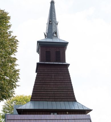 Zdjęcie nr 9: Kościół Przemienienia Pańskiego w Radoczy usytuowany jest w centrum wsi na zachód od głównej drogi prowadzącej z Wadowic do Zatora. Teren przykościelny jest usytuowany na niewielkim wzniesieniu, otoczony drewnianym płotem. Główne wejście na plac przykościelny prowadzi przez bramę od strony zachodniej.

Kościół jest orientowany, drewniany o konstrukcji zrębowej z wieżą na słup, jednonawowy z krótszym prezbiterium zamkniętym trójbocznie. Przy prezbiterium od wschodu nowsza zakrystia murowana, od północy kaplica i składzik, przy nawie od południa kruchta. Wnętrze nakryte pułapem, w nawie z zaskrzynieniami. Ściana arkady tęczowej o wykroju prostokątnym ze ściętymi narożami. Do kościoła prowadzi główne wejście w wieży od strony północnej. Wnętrze świątyni oświetlają prostokątne okna od strony południowej. Dach o jednej kalenicy, kryty blachą, na środku drewniana sygnaturka, nakryta kopułką z latarnią.  Od zachodu wieża w dolnej kondygnacji na planie prostokąta, ujęta po bokach daszkami; druga kondygnacja o ścianach pochyłych, pokryta gontem; trzecia kondygnacja prześwietlona prostokątnymi otworami okiennymi; wieża zakończona iglicą. Ściany na zewnątrz pokryte szalunkiem pionowym.
