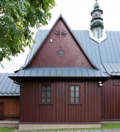 Zdjęcie nr 22: Kościół Przemienienia Pańskiego w Radoczy usytuowany jest w centrum wsi na zachód od głównej drogi prowadzącej z Wadowic do Zatora. Teren przykościelny jest usytuowany na niewielkim wzniesieniu, otoczony drewnianym płotem. Główne wejście na plac przykościelny prowadzi przez bramę od strony zachodniej.

Kościół jest orientowany, drewniany o konstrukcji zrębowej z wieżą na słup, jednonawowy z krótszym prezbiterium zamkniętym trójbocznie. Przy prezbiterium od wschodu nowsza zakrystia murowana, od północy kaplica i składzik, przy nawie od południa kruchta. Wnętrze nakryte pułapem, w nawie z zaskrzynieniami. Ściana arkady tęczowej o wykroju prostokątnym ze ściętymi narożami. Do kościoła prowadzi główne wejście w wieży od strony północnej. Wnętrze świątyni oświetlają prostokątne okna od strony południowej. Dach o jednej kalenicy, kryty blachą, na środku drewniana sygnaturka, nakryta kopułką z latarnią.  Od zachodu wieża w dolnej kondygnacji na planie prostokąta, ujęta po bokach daszkami; druga kondygnacja o ścianach pochyłych, pokryta gontem; trzecia kondygnacja prześwietlona prostokątnymi otworami okiennymi; wieża zakończona iglicą. Ściany na zewnątrz pokryte szalunkiem pionowym.
