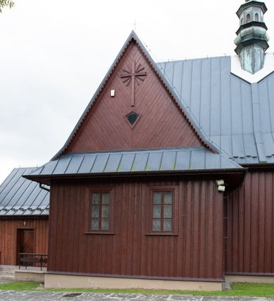 Zdjęcie nr 23: Kościół Przemienienia Pańskiego w Radoczy usytuowany jest w centrum wsi na zachód od głównej drogi prowadzącej z Wadowic do Zatora. Teren przykościelny jest usytuowany na niewielkim wzniesieniu, otoczony drewnianym płotem. Główne wejście na plac przykościelny prowadzi przez bramę od strony zachodniej.

Kościół jest orientowany, drewniany o konstrukcji zrębowej z wieżą na słup, jednonawowy z krótszym prezbiterium zamkniętym trójbocznie. Przy prezbiterium od wschodu nowsza zakrystia murowana, od północy kaplica i składzik, przy nawie od południa kruchta. Wnętrze nakryte pułapem, w nawie z zaskrzynieniami. Ściana arkady tęczowej o wykroju prostokątnym ze ściętymi narożami. Do kościoła prowadzi główne wejście w wieży od strony północnej. Wnętrze świątyni oświetlają prostokątne okna od strony południowej. Dach o jednej kalenicy, kryty blachą, na środku drewniana sygnaturka, nakryta kopułką z latarnią.  Od zachodu wieża w dolnej kondygnacji na planie prostokąta, ujęta po bokach daszkami; druga kondygnacja o ścianach pochyłych, pokryta gontem; trzecia kondygnacja prześwietlona prostokątnymi otworami okiennymi; wieża zakończona iglicą. Ściany na zewnątrz pokryte szalunkiem pionowym.
