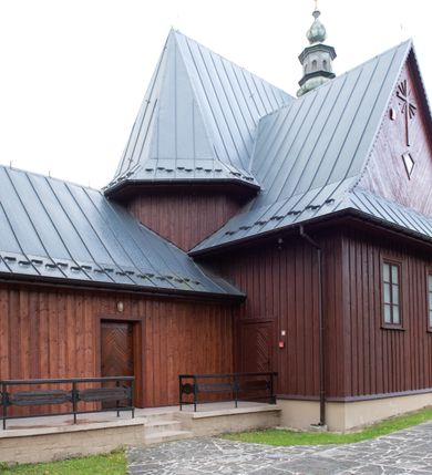 Zdjęcie nr 20: Kościół Przemienienia Pańskiego w Radoczy usytuowany jest w centrum wsi na zachód od głównej drogi prowadzącej z Wadowic do Zatora. Teren przykościelny jest usytuowany na niewielkim wzniesieniu, otoczony drewnianym płotem. Główne wejście na plac przykościelny prowadzi przez bramę od strony zachodniej.

Kościół jest orientowany, drewniany o konstrukcji zrębowej z wieżą na słup, jednonawowy z krótszym prezbiterium zamkniętym trójbocznie. Przy prezbiterium od wschodu nowsza zakrystia murowana, od północy kaplica i składzik, przy nawie od południa kruchta. Wnętrze nakryte pułapem, w nawie z zaskrzynieniami. Ściana arkady tęczowej o wykroju prostokątnym ze ściętymi narożami. Do kościoła prowadzi główne wejście w wieży od strony północnej. Wnętrze świątyni oświetlają prostokątne okna od strony południowej. Dach o jednej kalenicy, kryty blachą, na środku drewniana sygnaturka, nakryta kopułką z latarnią.  Od zachodu wieża w dolnej kondygnacji na planie prostokąta, ujęta po bokach daszkami; druga kondygnacja o ścianach pochyłych, pokryta gontem; trzecia kondygnacja prześwietlona prostokątnymi otworami okiennymi; wieża zakończona iglicą. Ściany na zewnątrz pokryte szalunkiem pionowym.
