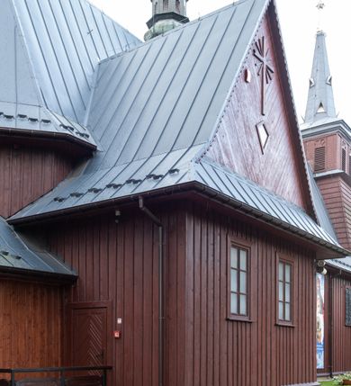 Zdjęcie nr 24: Kościół Przemienienia Pańskiego w Radoczy usytuowany jest w centrum wsi na zachód od głównej drogi prowadzącej z Wadowic do Zatora. Teren przykościelny jest usytuowany na niewielkim wzniesieniu, otoczony drewnianym płotem. Główne wejście na plac przykościelny prowadzi przez bramę od strony zachodniej.

Kościół jest orientowany, drewniany o konstrukcji zrębowej z wieżą na słup, jednonawowy z krótszym prezbiterium zamkniętym trójbocznie. Przy prezbiterium od wschodu nowsza zakrystia murowana, od północy kaplica i składzik, przy nawie od południa kruchta. Wnętrze nakryte pułapem, w nawie z zaskrzynieniami. Ściana arkady tęczowej o wykroju prostokątnym ze ściętymi narożami. Do kościoła prowadzi główne wejście w wieży od strony północnej. Wnętrze świątyni oświetlają prostokątne okna od strony południowej. Dach o jednej kalenicy, kryty blachą, na środku drewniana sygnaturka, nakryta kopułką z latarnią.  Od zachodu wieża w dolnej kondygnacji na planie prostokąta, ujęta po bokach daszkami; druga kondygnacja o ścianach pochyłych, pokryta gontem; trzecia kondygnacja prześwietlona prostokątnymi otworami okiennymi; wieża zakończona iglicą. Ściany na zewnątrz pokryte szalunkiem pionowym.
