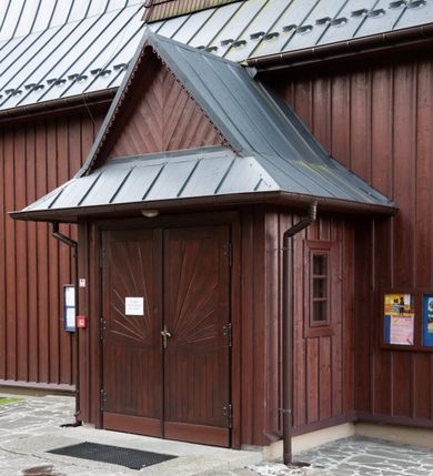 Zdjęcie nr 27: Kościół Przemienienia Pańskiego w Radoczy usytuowany jest w centrum wsi na zachód od głównej drogi prowadzącej z Wadowic do Zatora. Teren przykościelny jest usytuowany na niewielkim wzniesieniu, otoczony drewnianym płotem. Główne wejście na plac przykościelny prowadzi przez bramę od strony zachodniej.

Kościół jest orientowany, drewniany o konstrukcji zrębowej z wieżą na słup, jednonawowy z krótszym prezbiterium zamkniętym trójbocznie. Przy prezbiterium od wschodu nowsza zakrystia murowana, od północy kaplica i składzik, przy nawie od południa kruchta. Wnętrze nakryte pułapem, w nawie z zaskrzynieniami. Ściana arkady tęczowej o wykroju prostokątnym ze ściętymi narożami. Do kościoła prowadzi główne wejście w wieży od strony północnej. Wnętrze świątyni oświetlają prostokątne okna od strony południowej. Dach o jednej kalenicy, kryty blachą, na środku drewniana sygnaturka, nakryta kopułką z latarnią.  Od zachodu wieża w dolnej kondygnacji na planie prostokąta, ujęta po bokach daszkami; druga kondygnacja o ścianach pochyłych, pokryta gontem; trzecia kondygnacja prześwietlona prostokątnymi otworami okiennymi; wieża zakończona iglicą. Ściany na zewnątrz pokryte szalunkiem pionowym.
