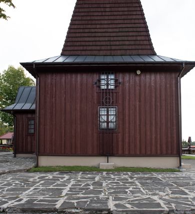 Zdjęcie nr 29: Kościół Przemienienia Pańskiego w Radoczy usytuowany jest w centrum wsi na zachód od głównej drogi prowadzącej z Wadowic do Zatora. Teren przykościelny jest usytuowany na niewielkim wzniesieniu, otoczony drewnianym płotem. Główne wejście na plac przykościelny prowadzi przez bramę od strony zachodniej.

Kościół jest orientowany, drewniany o konstrukcji zrębowej z wieżą na słup, jednonawowy z krótszym prezbiterium zamkniętym trójbocznie. Przy prezbiterium od wschodu nowsza zakrystia murowana, od północy kaplica i składzik, przy nawie od południa kruchta. Wnętrze nakryte pułapem, w nawie z zaskrzynieniami. Ściana arkady tęczowej o wykroju prostokątnym ze ściętymi narożami. Do kościoła prowadzi główne wejście w wieży od strony północnej. Wnętrze świątyni oświetlają prostokątne okna od strony południowej. Dach o jednej kalenicy, kryty blachą, na środku drewniana sygnaturka, nakryta kopułką z latarnią.  Od zachodu wieża w dolnej kondygnacji na planie prostokąta, ujęta po bokach daszkami; druga kondygnacja o ścianach pochyłych, pokryta gontem; trzecia kondygnacja prześwietlona prostokątnymi otworami okiennymi; wieża zakończona iglicą. Ściany na zewnątrz pokryte szalunkiem pionowym.
