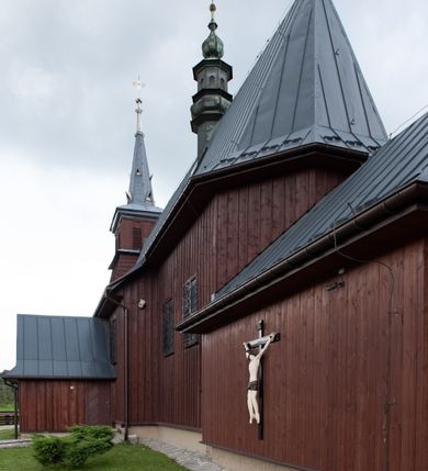 Zdjęcie nr 41: Kościół Przemienienia Pańskiego w Radoczy usytuowany jest w centrum wsi na zachód od głównej drogi prowadzącej z Wadowic do Zatora. Teren przykościelny jest usytuowany na niewielkim wzniesieniu, otoczony drewnianym płotem. Główne wejście na plac przykościelny prowadzi przez bramę od strony zachodniej.

Kościół jest orientowany, drewniany o konstrukcji zrębowej z wieżą na słup, jednonawowy z krótszym prezbiterium zamkniętym trójbocznie. Przy prezbiterium od wschodu nowsza zakrystia murowana, od północy kaplica i składzik, przy nawie od południa kruchta. Wnętrze nakryte pułapem, w nawie z zaskrzynieniami. Ściana arkady tęczowej o wykroju prostokątnym ze ściętymi narożami. Do kościoła prowadzi główne wejście w wieży od strony północnej. Wnętrze świątyni oświetlają prostokątne okna od strony południowej. Dach o jednej kalenicy, kryty blachą, na środku drewniana sygnaturka, nakryta kopułką z latarnią.  Od zachodu wieża w dolnej kondygnacji na planie prostokąta, ujęta po bokach daszkami; druga kondygnacja o ścianach pochyłych, pokryta gontem; trzecia kondygnacja prześwietlona prostokątnymi otworami okiennymi; wieża zakończona iglicą. Ściany na zewnątrz pokryte szalunkiem pionowym.
