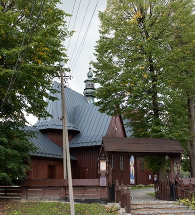 Zdjęcie nr 47: Kościół Przemienienia Pańskiego w Radoczy usytuowany jest w centrum wsi na zachód od głównej drogi prowadzącej z Wadowic do Zatora. Teren przykościelny jest usytuowany na niewielkim wzniesieniu, otoczony drewnianym płotem. Główne wejście na plac przykościelny prowadzi przez bramę od strony zachodniej.

Kościół jest orientowany, drewniany o konstrukcji zrębowej z wieżą na słup, jednonawowy z krótszym prezbiterium zamkniętym trójbocznie. Przy prezbiterium od wschodu nowsza zakrystia murowana, od północy kaplica i składzik, przy nawie od południa kruchta. Wnętrze nakryte pułapem, w nawie z zaskrzynieniami. Ściana arkady tęczowej o wykroju prostokątnym ze ściętymi narożami. Do kościoła prowadzi główne wejście w wieży od strony północnej. Wnętrze świątyni oświetlają prostokątne okna od strony południowej. Dach o jednej kalenicy, kryty blachą, na środku drewniana sygnaturka, nakryta kopułką z latarnią.  Od zachodu wieża w dolnej kondygnacji na planie prostokąta, ujęta po bokach daszkami; druga kondygnacja o ścianach pochyłych, pokryta gontem; trzecia kondygnacja prześwietlona prostokątnymi otworami okiennymi; wieża zakończona iglicą. Ściany na zewnątrz pokryte szalunkiem pionowym.
