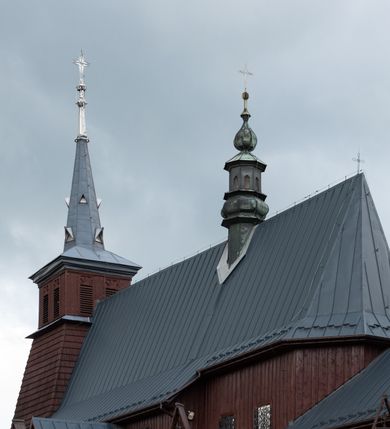 Zdjęcie nr 48: Kościół Przemienienia Pańskiego w Radoczy usytuowany jest w centrum wsi na zachód od głównej drogi prowadzącej z Wadowic do Zatora. Teren przykościelny jest usytuowany na niewielkim wzniesieniu, otoczony drewnianym płotem. Główne wejście na plac przykościelny prowadzi przez bramę od strony zachodniej.

Kościół jest orientowany, drewniany o konstrukcji zrębowej z wieżą na słup, jednonawowy z krótszym prezbiterium zamkniętym trójbocznie. Przy prezbiterium od wschodu nowsza zakrystia murowana, od północy kaplica i składzik, przy nawie od południa kruchta. Wnętrze nakryte pułapem, w nawie z zaskrzynieniami. Ściana arkady tęczowej o wykroju prostokątnym ze ściętymi narożami. Do kościoła prowadzi główne wejście w wieży od strony północnej. Wnętrze świątyni oświetlają prostokątne okna od strony południowej. Dach o jednej kalenicy, kryty blachą, na środku drewniana sygnaturka, nakryta kopułką z latarnią.  Od zachodu wieża w dolnej kondygnacji na planie prostokąta, ujęta po bokach daszkami; druga kondygnacja o ścianach pochyłych, pokryta gontem; trzecia kondygnacja prześwietlona prostokątnymi otworami okiennymi; wieża zakończona iglicą. Ściany na zewnątrz pokryte szalunkiem pionowym.
