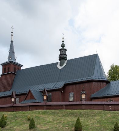 Zdjęcie nr 52: Kościół Przemienienia Pańskiego w Radoczy usytuowany jest w centrum wsi na zachód od głównej drogi prowadzącej z Wadowic do Zatora. Teren przykościelny jest usytuowany na niewielkim wzniesieniu, otoczony drewnianym płotem. Główne wejście na plac przykościelny prowadzi przez bramę od strony zachodniej.

Kościół jest orientowany, drewniany o konstrukcji zrębowej z wieżą na słup, jednonawowy z krótszym prezbiterium zamkniętym trójbocznie. Przy prezbiterium od wschodu nowsza zakrystia murowana, od północy kaplica i składzik, przy nawie od południa kruchta. Wnętrze nakryte pułapem, w nawie z zaskrzynieniami. Ściana arkady tęczowej o wykroju prostokątnym ze ściętymi narożami. Do kościoła prowadzi główne wejście w wieży od strony północnej. Wnętrze świątyni oświetlają prostokątne okna od strony południowej. Dach o jednej kalenicy, kryty blachą, na środku drewniana sygnaturka, nakryta kopułką z latarnią.  Od zachodu wieża w dolnej kondygnacji na planie prostokąta, ujęta po bokach daszkami; druga kondygnacja o ścianach pochyłych, pokryta gontem; trzecia kondygnacja prześwietlona prostokątnymi otworami okiennymi; wieża zakończona iglicą. Ściany na zewnątrz pokryte szalunkiem pionowym.
