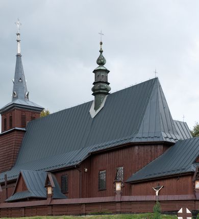 Zdjęcie nr 49: Kościół Przemienienia Pańskiego w Radoczy usytuowany jest w centrum wsi na zachód od głównej drogi prowadzącej z Wadowic do Zatora. Teren przykościelny jest usytuowany na niewielkim wzniesieniu, otoczony drewnianym płotem. Główne wejście na plac przykościelny prowadzi przez bramę od strony zachodniej.

Kościół jest orientowany, drewniany o konstrukcji zrębowej z wieżą na słup, jednonawowy z krótszym prezbiterium zamkniętym trójbocznie. Przy prezbiterium od wschodu nowsza zakrystia murowana, od północy kaplica i składzik, przy nawie od południa kruchta. Wnętrze nakryte pułapem, w nawie z zaskrzynieniami. Ściana arkady tęczowej o wykroju prostokątnym ze ściętymi narożami. Do kościoła prowadzi główne wejście w wieży od strony północnej. Wnętrze świątyni oświetlają prostokątne okna od strony południowej. Dach o jednej kalenicy, kryty blachą, na środku drewniana sygnaturka, nakryta kopułką z latarnią.  Od zachodu wieża w dolnej kondygnacji na planie prostokąta, ujęta po bokach daszkami; druga kondygnacja o ścianach pochyłych, pokryta gontem; trzecia kondygnacja prześwietlona prostokątnymi otworami okiennymi; wieża zakończona iglicą. Ściany na zewnątrz pokryte szalunkiem pionowym.
