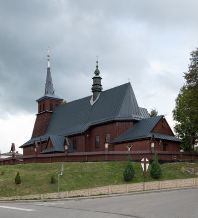 Zdjęcie nr 54: Kościół Przemienienia Pańskiego w Radoczy usytuowany jest w centrum wsi na zachód od głównej drogi prowadzącej z Wadowic do Zatora. Teren przykościelny jest usytuowany na niewielkim wzniesieniu, otoczony drewnianym płotem. Główne wejście na plac przykościelny prowadzi przez bramę od strony zachodniej.

Kościół jest orientowany, drewniany o konstrukcji zrębowej z wieżą na słup, jednonawowy z krótszym prezbiterium zamkniętym trójbocznie. Przy prezbiterium od wschodu nowsza zakrystia murowana, od północy kaplica i składzik, przy nawie od południa kruchta. Wnętrze nakryte pułapem, w nawie z zaskrzynieniami. Ściana arkady tęczowej o wykroju prostokątnym ze ściętymi narożami. Do kościoła prowadzi główne wejście w wieży od strony północnej. Wnętrze świątyni oświetlają prostokątne okna od strony południowej. Dach o jednej kalenicy, kryty blachą, na środku drewniana sygnaturka, nakryta kopułką z latarnią.  Od zachodu wieża w dolnej kondygnacji na planie prostokąta, ujęta po bokach daszkami; druga kondygnacja o ścianach pochyłych, pokryta gontem; trzecia kondygnacja prześwietlona prostokątnymi otworami okiennymi; wieża zakończona iglicą. Ściany na zewnątrz pokryte szalunkiem pionowym.
