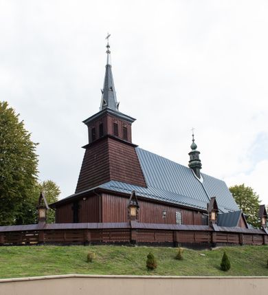 Zdjęcie nr 56: Kościół Przemienienia Pańskiego w Radoczy usytuowany jest w centrum wsi na zachód od głównej drogi prowadzącej z Wadowic do Zatora. Teren przykościelny jest usytuowany na niewielkim wzniesieniu, otoczony drewnianym płotem. Główne wejście na plac przykościelny prowadzi przez bramę od strony zachodniej.

Kościół jest orientowany, drewniany o konstrukcji zrębowej z wieżą na słup, jednonawowy z krótszym prezbiterium zamkniętym trójbocznie. Przy prezbiterium od wschodu nowsza zakrystia murowana, od północy kaplica i składzik, przy nawie od południa kruchta. Wnętrze nakryte pułapem, w nawie z zaskrzynieniami. Ściana arkady tęczowej o wykroju prostokątnym ze ściętymi narożami. Do kościoła prowadzi główne wejście w wieży od strony północnej. Wnętrze świątyni oświetlają prostokątne okna od strony południowej. Dach o jednej kalenicy, kryty blachą, na środku drewniana sygnaturka, nakryta kopułką z latarnią.  Od zachodu wieża w dolnej kondygnacji na planie prostokąta, ujęta po bokach daszkami; druga kondygnacja o ścianach pochyłych, pokryta gontem; trzecia kondygnacja prześwietlona prostokątnymi otworami okiennymi; wieża zakończona iglicą. Ściany na zewnątrz pokryte szalunkiem pionowym.
