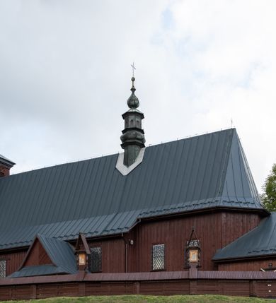 Zdjęcie nr 53: Kościół Przemienienia Pańskiego w Radoczy usytuowany jest w centrum wsi na zachód od głównej drogi prowadzącej z Wadowic do Zatora. Teren przykościelny jest usytuowany na niewielkim wzniesieniu, otoczony drewnianym płotem. Główne wejście na plac przykościelny prowadzi przez bramę od strony zachodniej.

Kościół jest orientowany, drewniany o konstrukcji zrębowej z wieżą na słup, jednonawowy z krótszym prezbiterium zamkniętym trójbocznie. Przy prezbiterium od wschodu nowsza zakrystia murowana, od północy kaplica i składzik, przy nawie od południa kruchta. Wnętrze nakryte pułapem, w nawie z zaskrzynieniami. Ściana arkady tęczowej o wykroju prostokątnym ze ściętymi narożami. Do kościoła prowadzi główne wejście w wieży od strony północnej. Wnętrze świątyni oświetlają prostokątne okna od strony południowej. Dach o jednej kalenicy, kryty blachą, na środku drewniana sygnaturka, nakryta kopułką z latarnią.  Od zachodu wieża w dolnej kondygnacji na planie prostokąta, ujęta po bokach daszkami; druga kondygnacja o ścianach pochyłych, pokryta gontem; trzecia kondygnacja prześwietlona prostokątnymi otworami okiennymi; wieża zakończona iglicą. Ściany na zewnątrz pokryte szalunkiem pionowym.
