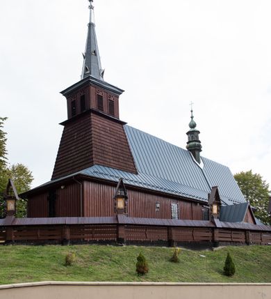 Zdjęcie nr 55: Kościół Przemienienia Pańskiego w Radoczy usytuowany jest w centrum wsi na zachód od głównej drogi prowadzącej z Wadowic do Zatora. Teren przykościelny jest usytuowany na niewielkim wzniesieniu, otoczony drewnianym płotem. Główne wejście na plac przykościelny prowadzi przez bramę od strony zachodniej.

Kościół jest orientowany, drewniany o konstrukcji zrębowej z wieżą na słup, jednonawowy z krótszym prezbiterium zamkniętym trójbocznie. Przy prezbiterium od wschodu nowsza zakrystia murowana, od północy kaplica i składzik, przy nawie od południa kruchta. Wnętrze nakryte pułapem, w nawie z zaskrzynieniami. Ściana arkady tęczowej o wykroju prostokątnym ze ściętymi narożami. Do kościoła prowadzi główne wejście w wieży od strony północnej. Wnętrze świątyni oświetlają prostokątne okna od strony południowej. Dach o jednej kalenicy, kryty blachą, na środku drewniana sygnaturka, nakryta kopułką z latarnią.  Od zachodu wieża w dolnej kondygnacji na planie prostokąta, ujęta po bokach daszkami; druga kondygnacja o ścianach pochyłych, pokryta gontem; trzecia kondygnacja prześwietlona prostokątnymi otworami okiennymi; wieża zakończona iglicą. Ściany na zewnątrz pokryte szalunkiem pionowym.
