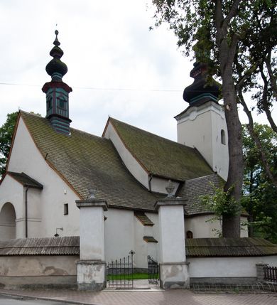 Zdjęcie nr 3: Kościół orientowany, murowany z kamienia, jednonawowy, z prostokątną, trójprzęsłową nawą oraz węższym dwuprzęsłowym prezbiterium zamkniętym prosto, z prostokątną zakrystią przy północnej ścianie. Od zachodu wieża na planie kwadratu, do północnej ściany nawy dobudowana kaplica na rzucie kwadratu o ściętych narożach, do południowej niewielka kruchta na planie kwadratu. Prezbiterium nakryte sklepieniem krzyżowo-żebrowym z dwoma zwornikami. 
Nawa sklepiona krzyżowo, przęsła wydzielone arkadami wspartymi na półfilarach. Otwór tęczowy w formie stojącego prostokąta zamkniętego łukiem półkolistym. W zachodniej części nawy parapet chóru muzycznego, z wybrzuszoną środkową częścią balustrady, wsparty na czterech kolumnach. 
Fasada wieżowa, z wejściem na osi. Wieża smukła, bez podziałów architektonicznych, zakończona profilowanym gzymsem, wyłamującym się na każdej ścianie na kształt łuku odcinkowego. W najwyższej partii ścian, z trzech stron, okna w formie stojącego prostokąta zamkniętego półkoliście. Wieża zwieńczona hełmem baniastym z latarnią, pokrytym gontem. 
Kościół opięty szkarpami dwuuskokowymi, nakrytymi daszkami gontowymi. W elewacji południowej pomiędzy szkarpami pięć wąskich okien w formie stojącego prostokąta zamkniętego łukiem półkolistym. Na wschodniej dobudowany ogrojec w formie masywnej arkady, zamkniętej dwuspadowym daszkiem z ołtarzem i krucyfiksem. Nawa i prezbiterium nakryte osobnymi dachami dwuspadowymi, gontowymi. Nad prezbiterium drewniana wieżyczka na sygnaturkę, z latarnią, zwieńczona hełmem baniastym. Kaplica przykryta dachem gontowych, trójspadowym, kruchta zaś pulpitowym. 
Kościół otoczony niskim murem kamiennym, nakrytym daszkiem gontowym. Od wschodu dwie bramy flankowane filarami z wazonami. 

