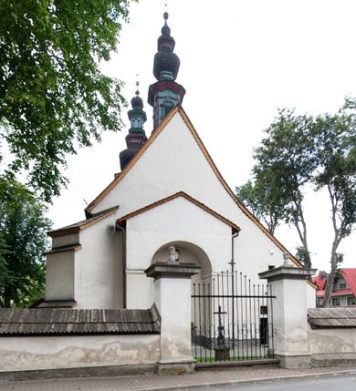 Zdjęcie nr 26: Kościół orientowany, murowany z kamienia, jednonawowy, z prostokątną, trójprzęsłową nawą oraz węższym dwuprzęsłowym prezbiterium zamkniętym prosto, z prostokątną zakrystią przy północnej ścianie. Od zachodu wieża na planie kwadratu, do północnej ściany nawy dobudowana kaplica na rzucie kwadratu o ściętych narożach, do południowej niewielka kruchta na planie kwadratu. Prezbiterium nakryte sklepieniem krzyżowo-żebrowym z dwoma zwornikami. 
Nawa sklepiona krzyżowo, przęsła wydzielone arkadami wspartymi na półfilarach. Otwór tęczowy w formie stojącego prostokąta zamkniętego łukiem półkolistym. W zachodniej części nawy parapet chóru muzycznego, z wybrzuszoną środkową częścią balustrady, wsparty na czterech kolumnach. 
Fasada wieżowa, z wejściem na osi. Wieża smukła, bez podziałów architektonicznych, zakończona profilowanym gzymsem, wyłamującym się na każdej ścianie na kształt łuku odcinkowego. W najwyższej partii ścian, z trzech stron, okna w formie stojącego prostokąta zamkniętego półkoliście. Wieża zwieńczona hełmem baniastym z latarnią, pokrytym gontem. 
Kościół opięty szkarpami dwuuskokowymi, nakrytymi daszkami gontowymi. W elewacji południowej pomiędzy szkarpami pięć wąskich okien w formie stojącego prostokąta zamkniętego łukiem półkolistym. Na wschodniej dobudowany ogrojec w formie masywnej arkady, zamkniętej dwuspadowym daszkiem z ołtarzem i krucyfiksem. Nawa i prezbiterium nakryte osobnymi dachami dwuspadowymi, gontowymi. Nad prezbiterium drewniana wieżyczka na sygnaturkę, z latarnią, zwieńczona hełmem baniastym. Kaplica przykryta dachem gontowych, trójspadowym, kruchta zaś pulpitowym. 
Kościół otoczony niskim murem kamiennym, nakrytym daszkiem gontowym. Od wschodu dwie bramy flankowane filarami z wazonami. 

