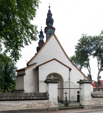 Zdjęcie nr 25: Kościół orientowany, murowany z kamienia, jednonawowy, z prostokątną, trójprzęsłową nawą oraz węższym dwuprzęsłowym prezbiterium zamkniętym prosto, z prostokątną zakrystią przy północnej ścianie. Od zachodu wieża na planie kwadratu, do północnej ściany nawy dobudowana kaplica na rzucie kwadratu o ściętych narożach, do południowej niewielka kruchta na planie kwadratu. Prezbiterium nakryte sklepieniem krzyżowo-żebrowym z dwoma zwornikami. 
Nawa sklepiona krzyżowo, przęsła wydzielone arkadami wspartymi na półfilarach. Otwór tęczowy w formie stojącego prostokąta zamkniętego łukiem półkolistym. W zachodniej części nawy parapet chóru muzycznego, z wybrzuszoną środkową częścią balustrady, wsparty na czterech kolumnach. 
Fasada wieżowa, z wejściem na osi. Wieża smukła, bez podziałów architektonicznych, zakończona profilowanym gzymsem, wyłamującym się na każdej ścianie na kształt łuku odcinkowego. W najwyższej partii ścian, z trzech stron, okna w formie stojącego prostokąta zamkniętego półkoliście. Wieża zwieńczona hełmem baniastym z latarnią, pokrytym gontem. 
Kościół opięty szkarpami dwuuskokowymi, nakrytymi daszkami gontowymi. W elewacji południowej pomiędzy szkarpami pięć wąskich okien w formie stojącego prostokąta zamkniętego łukiem półkolistym. Na wschodniej dobudowany ogrojec w formie masywnej arkady, zamkniętej dwuspadowym daszkiem z ołtarzem i krucyfiksem. Nawa i prezbiterium nakryte osobnymi dachami dwuspadowymi, gontowymi. Nad prezbiterium drewniana wieżyczka na sygnaturkę, z latarnią, zwieńczona hełmem baniastym. Kaplica przykryta dachem gontowych, trójspadowym, kruchta zaś pulpitowym. 
Kościół otoczony niskim murem kamiennym, nakrytym daszkiem gontowym. Od wschodu dwie bramy flankowane filarami z wazonami. 

