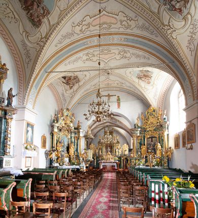 Zdjęcie nr 5: Kościół orientowany, murowany z kamienia, jednonawowy, z prostokątną, trójprzęsłową nawą oraz węższym dwuprzęsłowym prezbiterium zamkniętym prosto, z prostokątną zakrystią przy północnej ścianie. Od zachodu wieża na planie kwadratu, do północnej ściany nawy dobudowana kaplica na rzucie kwadratu o ściętych narożach, do południowej niewielka kruchta na planie kwadratu. Prezbiterium nakryte sklepieniem krzyżowo-żebrowym z dwoma zwornikami. 
Nawa sklepiona krzyżowo, przęsła wydzielone arkadami wspartymi na półfilarach. Otwór tęczowy w formie stojącego prostokąta zamkniętego łukiem półkolistym. W zachodniej części nawy parapet chóru muzycznego, z wybrzuszoną środkową częścią balustrady, wsparty na czterech kolumnach. 
Fasada wieżowa, z wejściem na osi. Wieża smukła, bez podziałów architektonicznych, zakończona profilowanym gzymsem, wyłamującym się na każdej ścianie na kształt łuku odcinkowego. W najwyższej partii ścian, z trzech stron, okna w formie stojącego prostokąta zamkniętego półkoliście. Wieża zwieńczona hełmem baniastym z latarnią, pokrytym gontem. 
Kościół opięty szkarpami dwuuskokowymi, nakrytymi daszkami gontowymi. W elewacji południowej pomiędzy szkarpami pięć wąskich okien w formie stojącego prostokąta zamkniętego łukiem półkolistym. Na wschodniej dobudowany ogrojec w formie masywnej arkady, zamkniętej dwuspadowym daszkiem z ołtarzem i krucyfiksem. Nawa i prezbiterium nakryte osobnymi dachami dwuspadowymi, gontowymi. Nad prezbiterium drewniana wieżyczka na sygnaturkę, z latarnią, zwieńczona hełmem baniastym. Kaplica przykryta dachem gontowych, trójspadowym, kruchta zaś pulpitowym. 
Kościół otoczony niskim murem kamiennym, nakrytym daszkiem gontowym. Od wschodu dwie bramy flankowane filarami z wazonami. 

